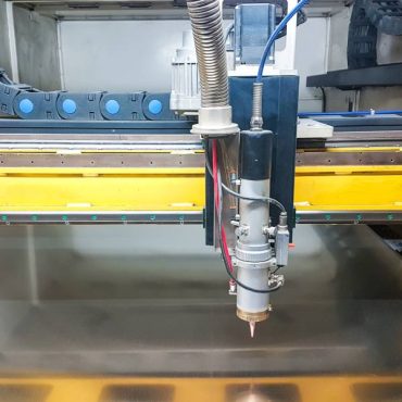 A laser machine working with a piece of metal. The laser machine is getting ready to dispense plasma surface treatment.